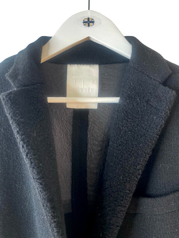 A close-up of a dark charcoal gray wool-blend coat with a plush sherpa lining, hanging on a white wooden hanger against a plain white background.