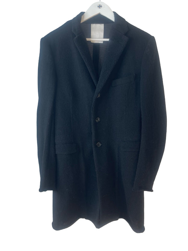 A black wool-blend coat with notch lapels, a three-button front closure, and flap pockets, hanging on a white hanger against a white background.