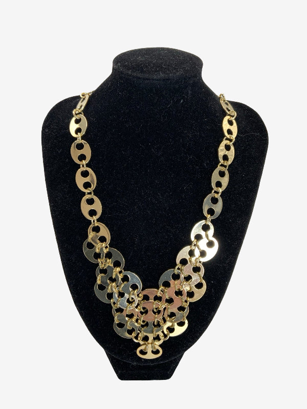 A chunky statement necklace made of interlocking circular links in gold and silver tones, displayed on a black velvet jewelry bust against a light gray background.