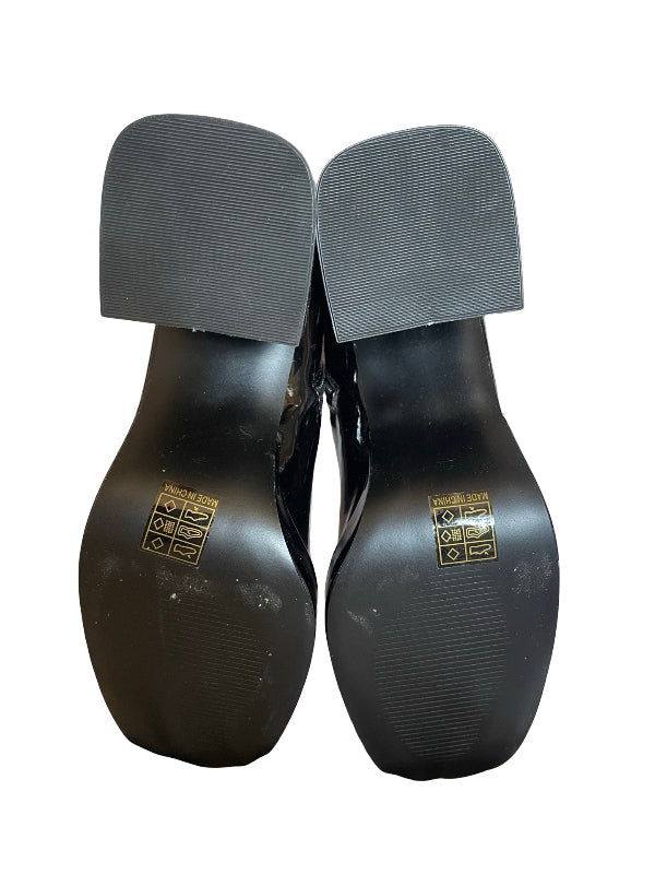 A pair of black patent leather shoes shown from the sole, featuring a rounded toe and a textured dark gray heel counter, with gold brand lettering on the soles.