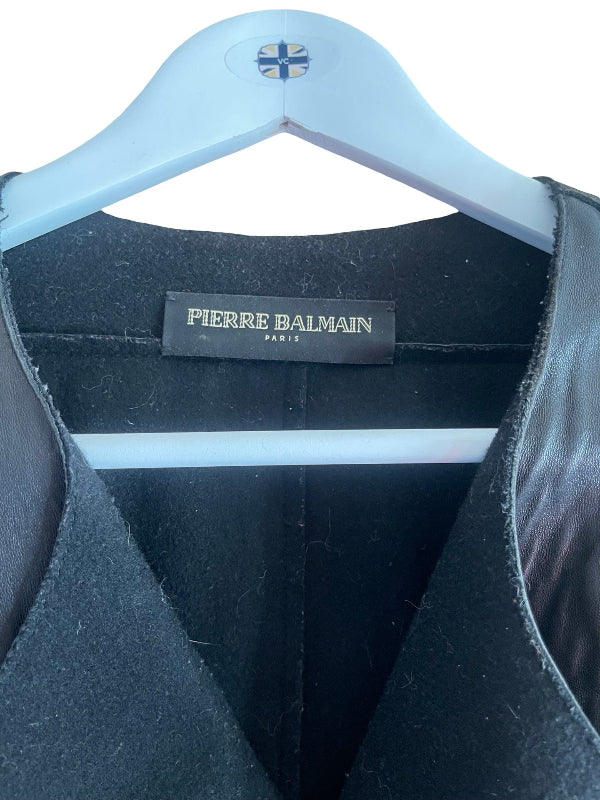 Close-up of a black Pierre Balmain coat or jacket hanging on a white hanger, showing the interior neck label and dark fabric texture.