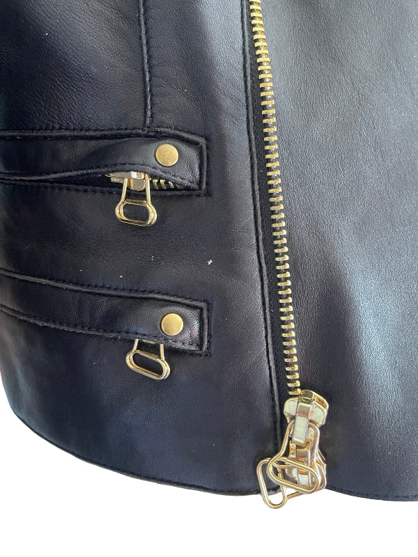 Close-up of a black leather bag featuring a vertical gold zipper and two zippered pockets with gold-tone metal snaps and pull tabs, set against a plain white background.