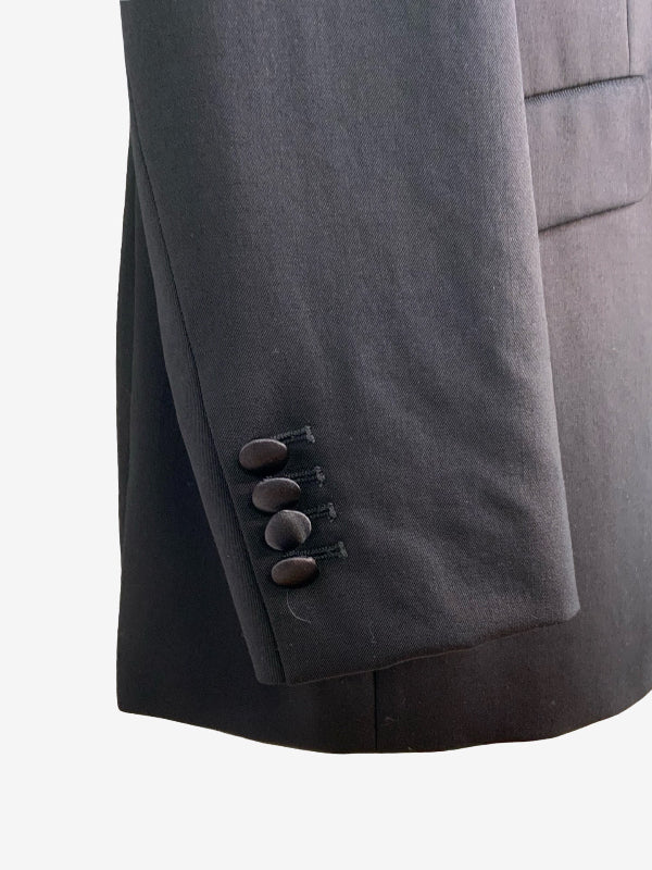 Close-up of a black tuxedo  jacket sleeve, showing four dark buttons on the cuff and a clean white background.
