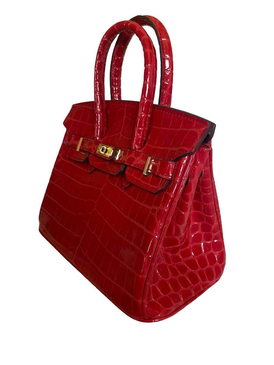 A red crocodile-embossed leather handbag with gold-tone hardware, shown on a plain white background.