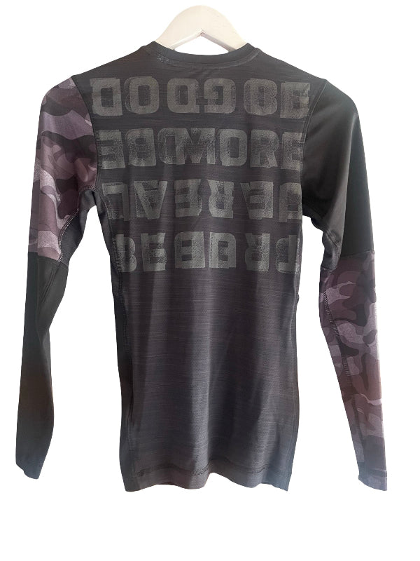 A long-sleeve athletic shirt hanging on a white hanger against a white background. The shirt is dark gray with a large gray text graphic on the back reading 'Be Good, be more, be real ' and features a camouflage pattern on the sleeves.