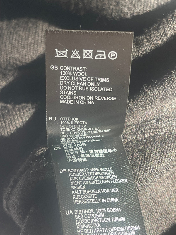 A close-up of a black garment care label with white text, photographed against dark textured fabric.