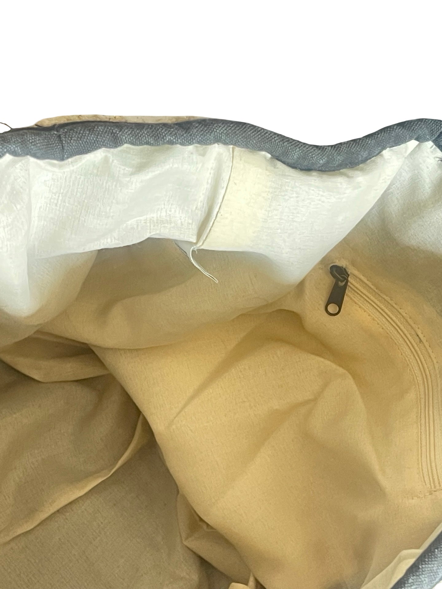 Close-up of the interior of a beige fabric bag or pouch, showing a cream-colored lining, a gray zipper track, and a small metal zipper pull.