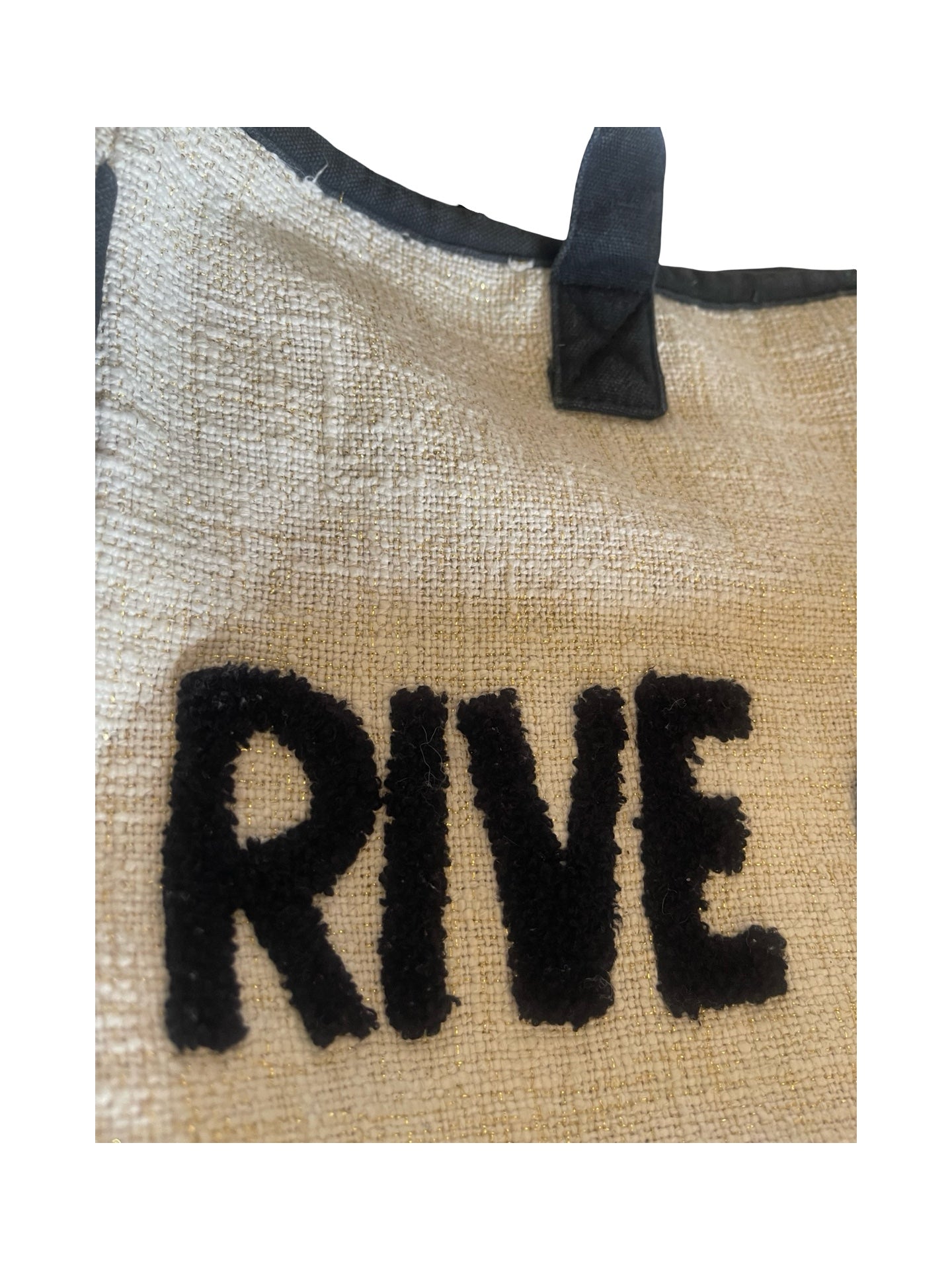 Close-up of a beige woven tote bag with black trim and black lettering that reads 'RIVE' on the front.