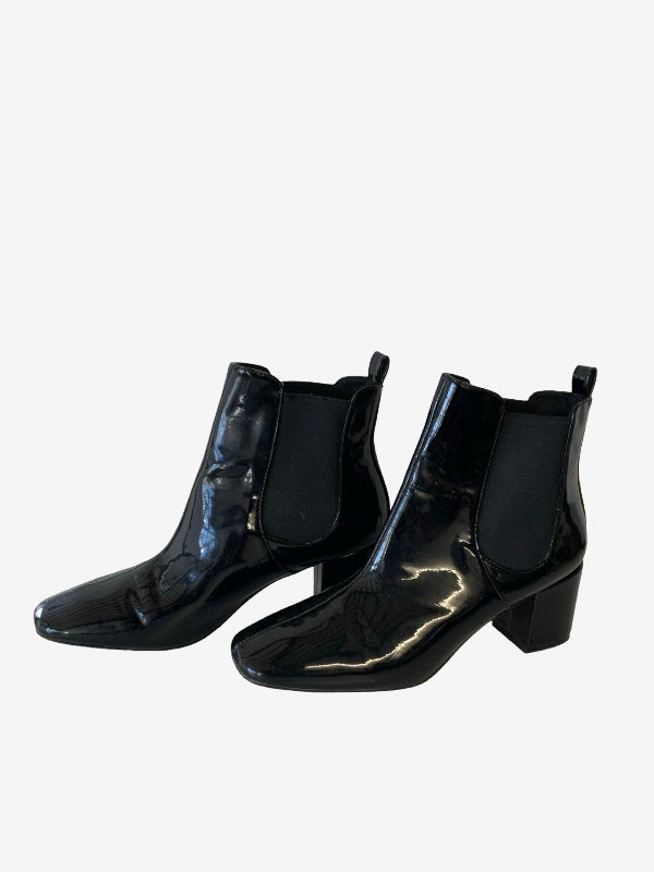 A pair of black patent leather ankle boots with elastic side panels and block heels, displayed against a plain light gray background.