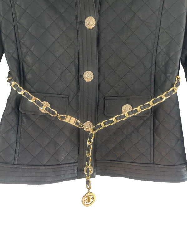 A black quilted leather jacket with gold-tone buttons and a matching gold chain belt featuring a circular monogram charm, shown against a plain white background.