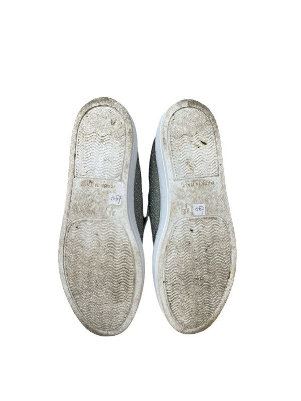 A pair of worn-out gray slip-on shoes shown from the bottom, highlighting slightly stained  rubber soles, against a plain white background.