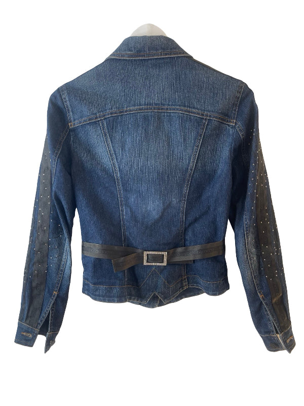 A blue denim jacket shown from the back on a mannequin, featuring a dark gray belt at the waist and silver stud embellishments on the sleeves, set against a plain white background.