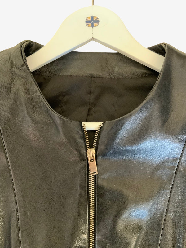 A close-up of a black leather jacket hanging on a white wooden hanger with a small cross logo, showing a front zipper.