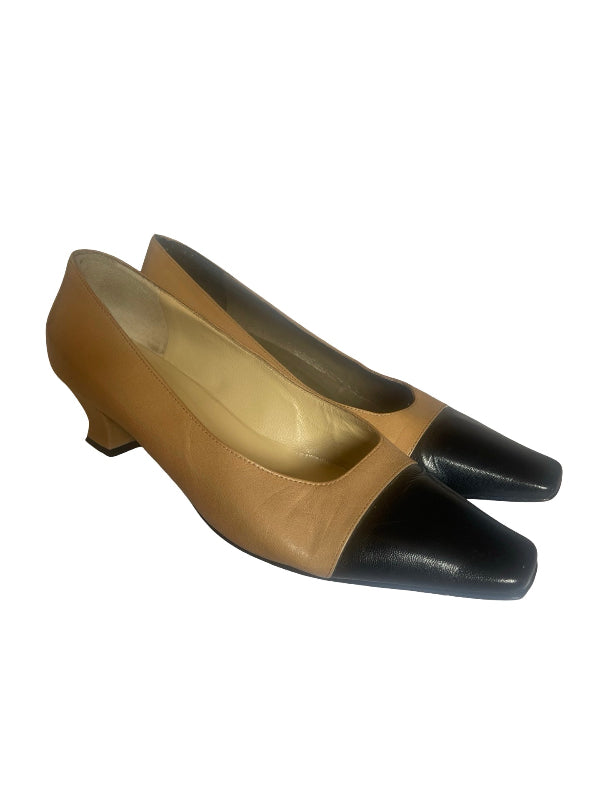 A pair of women's low-heel pumps with a two-tone color-blocked design, featuring a tan leather upper and a black leather pointed toe cap, shown against a plain white background.