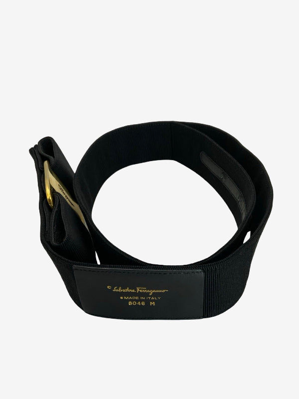 A black waist trainer belt with gold lettering, shown coiled on a light gray background. The brand 'Salvatore Ferragamo' is clearly printed in gold on the front.