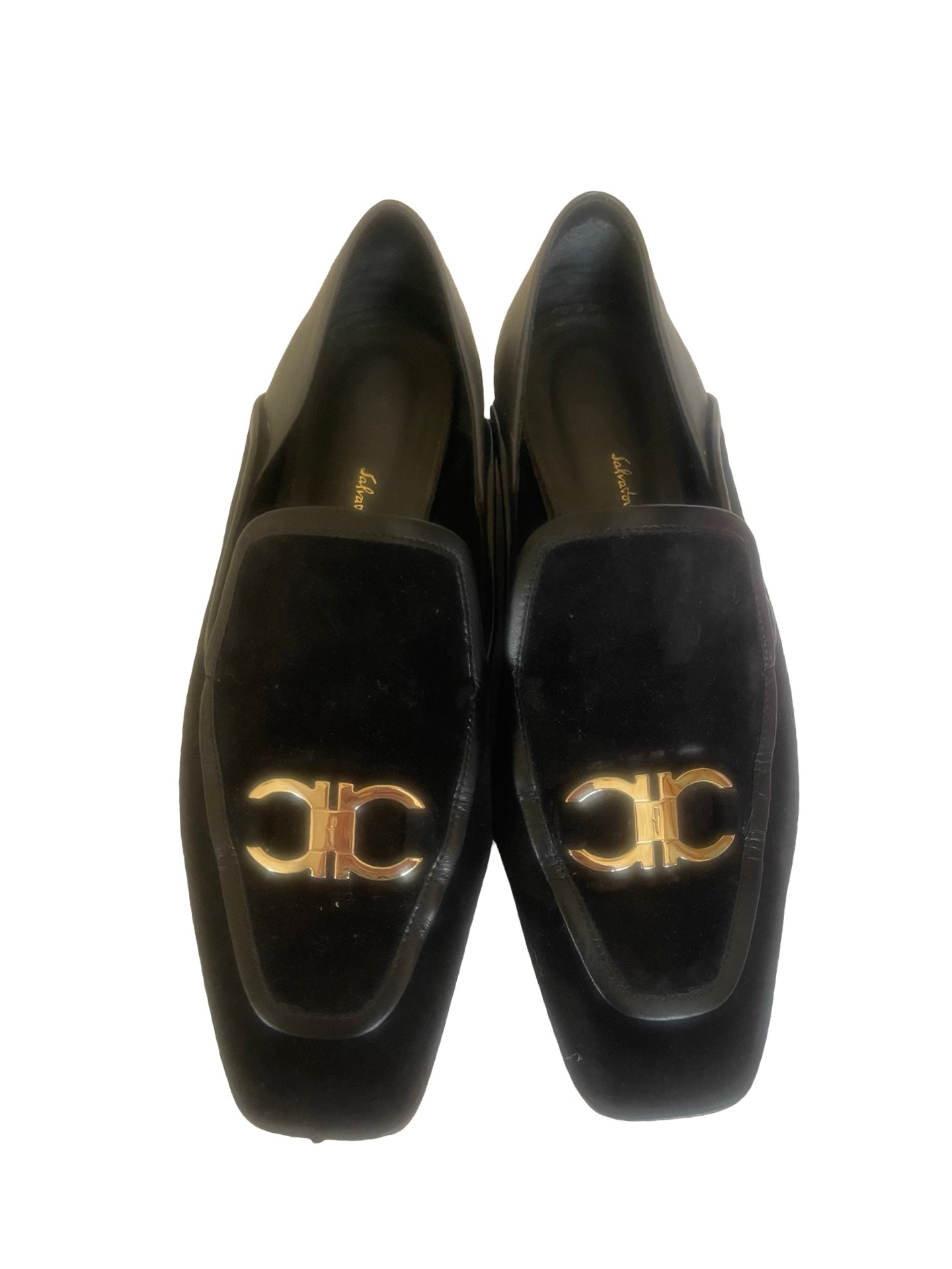 A pair of black leather loafers with a glossy finish and a prominent silver-tone double-C logo on the vamp, photographed from a top-down angle on a white background.