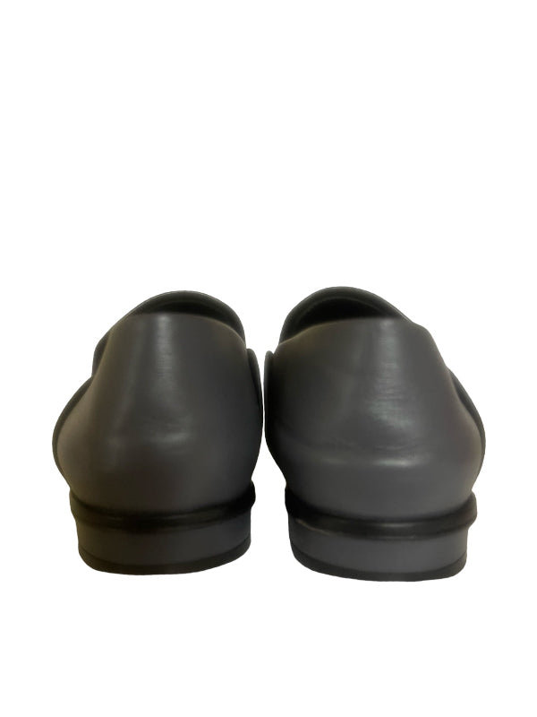 A pair of black and grey leather slip-on loafers shown from the back, featuring a smooth leather upper and a thick black sole, set against a plain white background.