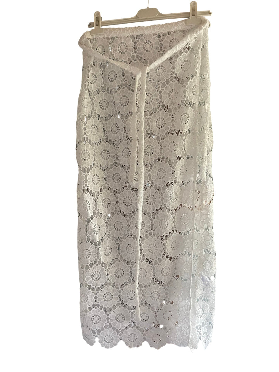 A white crochet lace midi skirt with a V-neckline and tie-front detail, hanging on a wooden hanger against a white background.