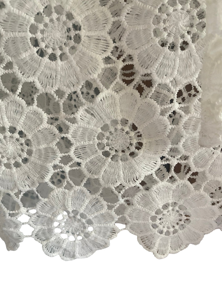 White floral lace fabric with intricate crocheted patterns and a scalloped edge, shown close-up against a white background.