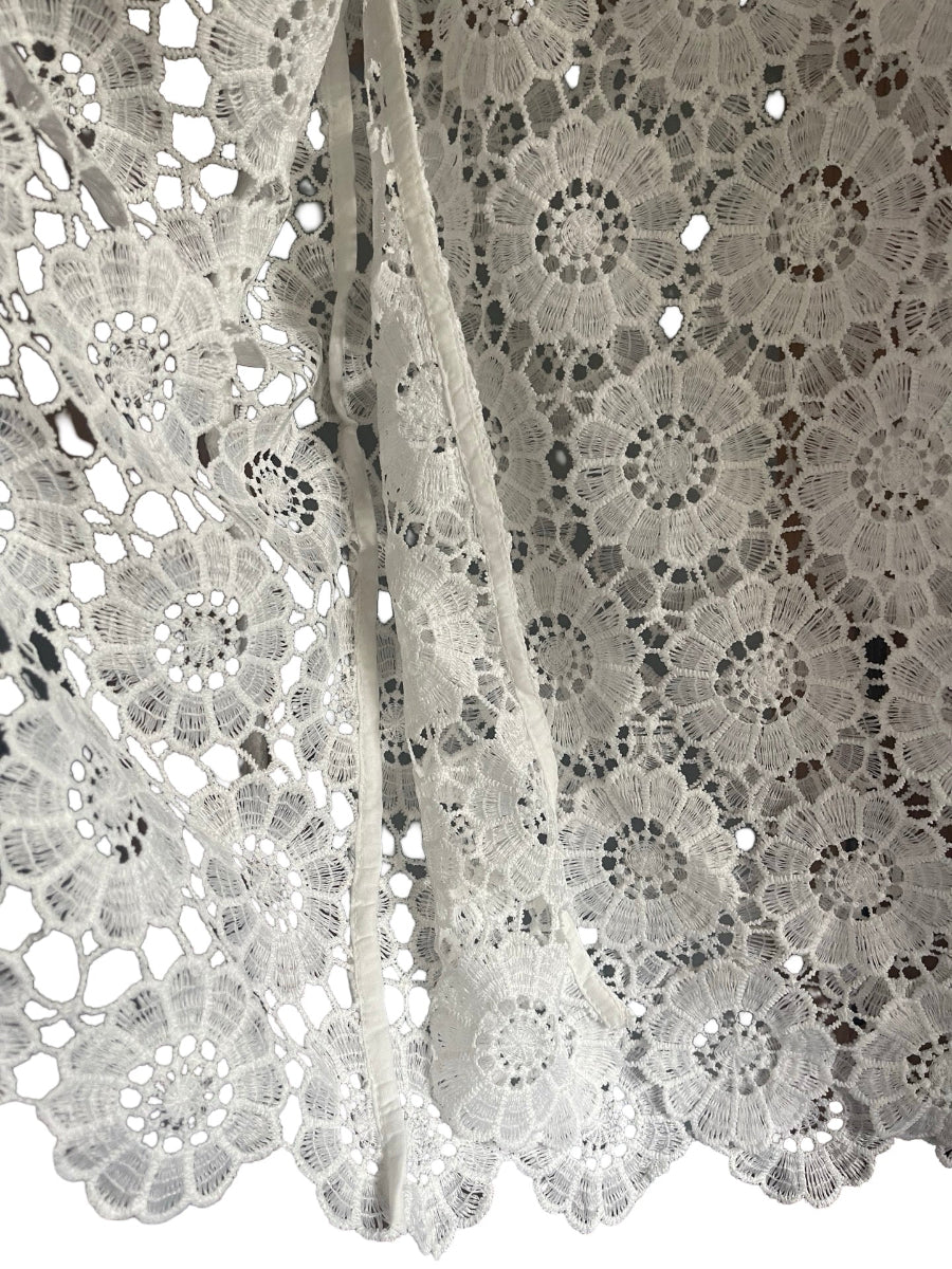 White floral lace fabric with intricate crochet patterns and scalloped edges, draped to show texture and detail.