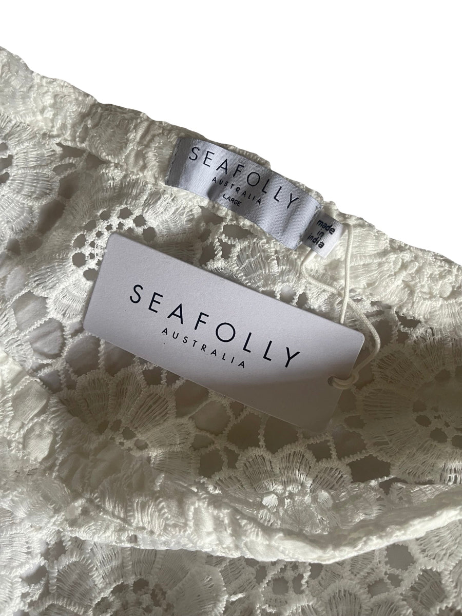 Close-up of a white lace garment with two visible SeaFolly Australia tags attached, showing the brand name and size information on a white background.