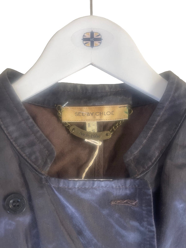 A close-up of a See By Chloe jacket hanging on a white hanger with the See By Chloe logo. The jacket has a dark gray-blue satin-like fabric exterior with a brown lining and a gold-tone brand label.