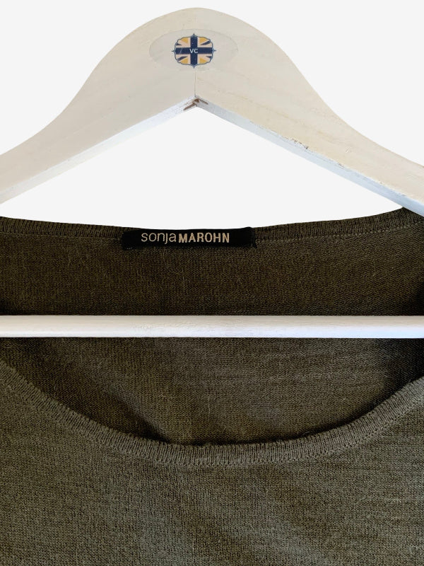 Close-up of an olive green knit top on a white wooden hanger, showing the black neck label with gold text 'sonja MAROHN' and a small blue-and-yellow cross logo at the top of the hanger.