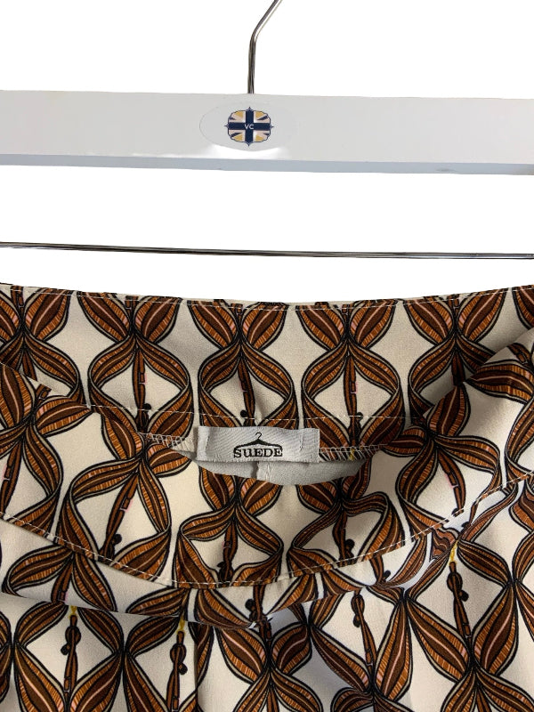 Close-up of a patterned garment hanging on a white hanger with a visible SUEDE waist  label. The fabric has an allover abstract leaf or floral motif in brown, black, and cream.