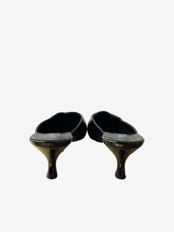 A pair of black leather mule heels with sculptural, tapered metallic gold mid-heel pumps, shown from the back on a light gray background.