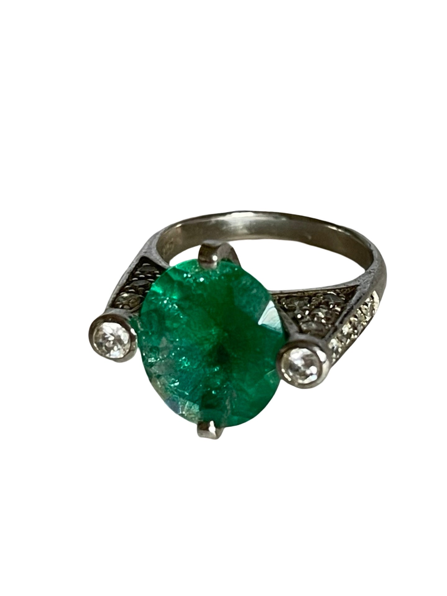 A silver ring featuring a large oval-cut green emerald gemstone in a prong setting, accented by two small round clear stones on the shoulders, shown against a plain white background.