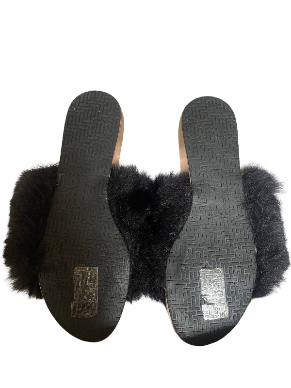 Black fur-trimmed slide sandals shown from the bottom, displaying the textured black soles with metallic brand patches on a white background.