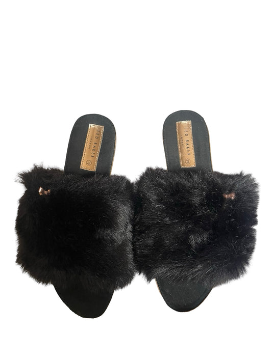 A pair of black fur-trimmed slide sandals with black soles and gold-tone brand plates, photographed against a plain white background.