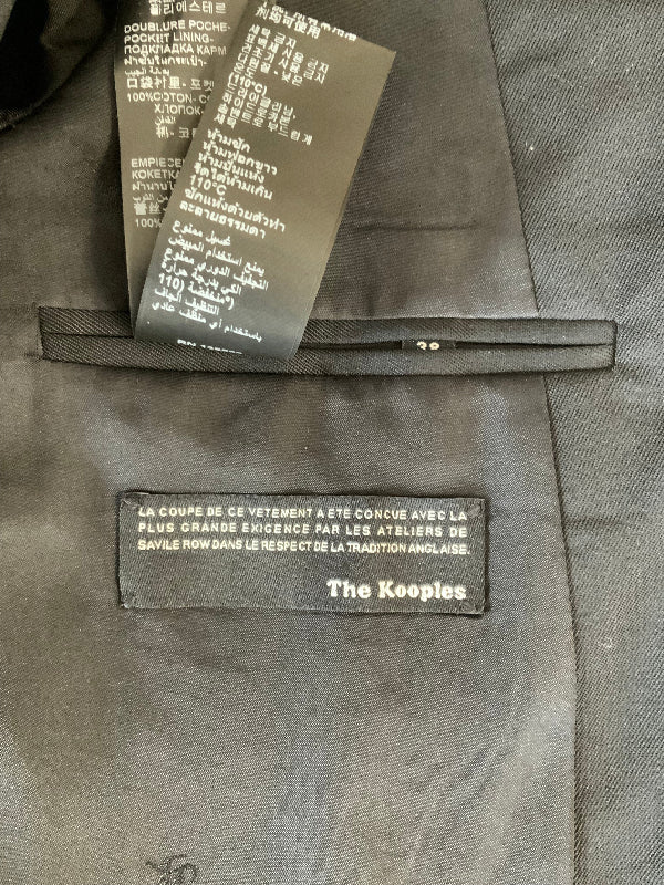 Close-up of a black tuxedo style  jacket interior showing a brand label reading 'The Kooples' and a hangtag with product details.