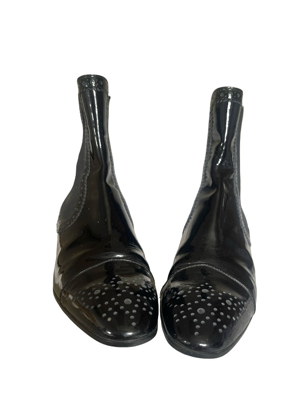 A pair of glossy black leather ankle boots with perforated detailing on the toes, shown against a plain white background.