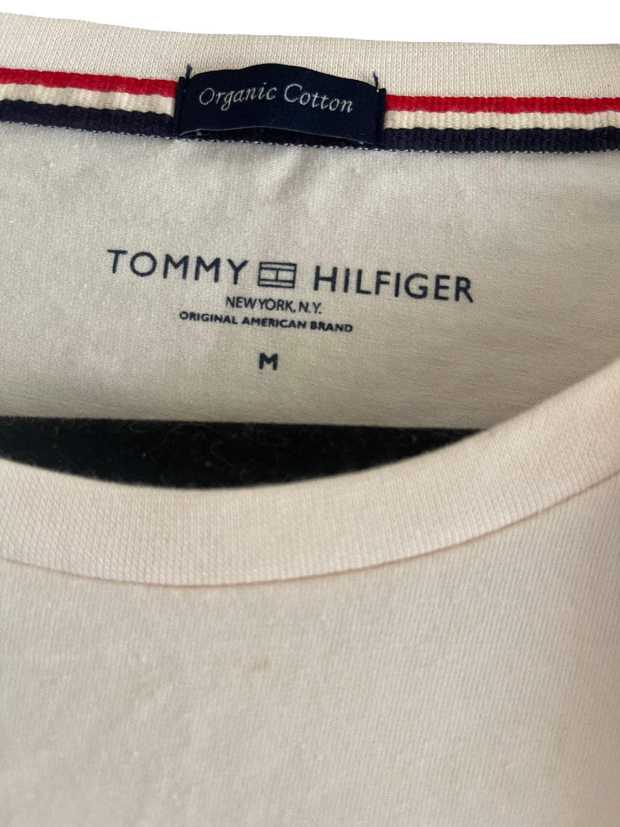Close-up of the inside collar of a Tommy Hilfiger crewneck shirt, showing the blush-colored fabric, a navy and red striped trim, and the brand name printed inside.