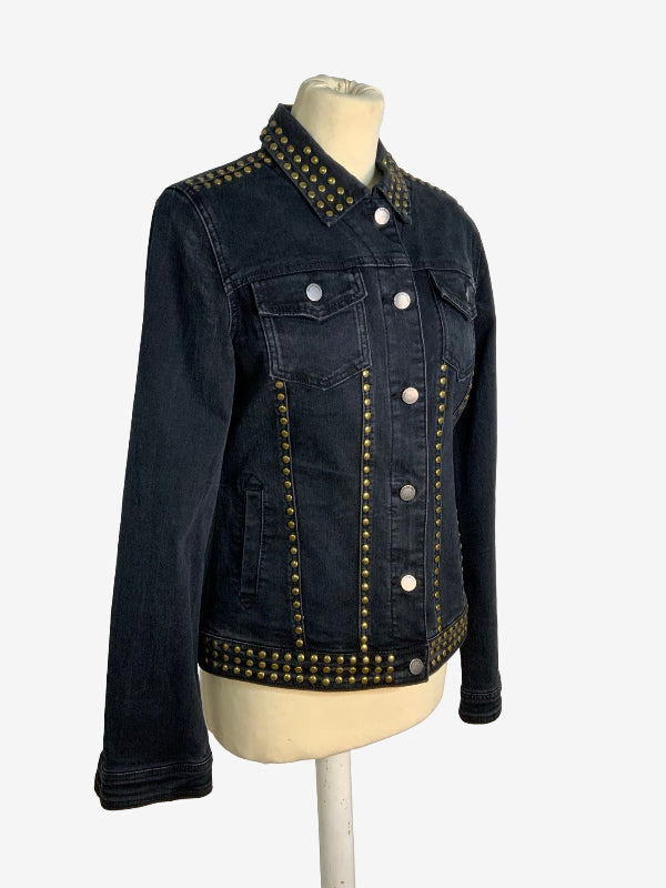 A dark wash denim jacket with gold-tone metal studs, displayed on a cream-colored mannequin torso against a light gray background.