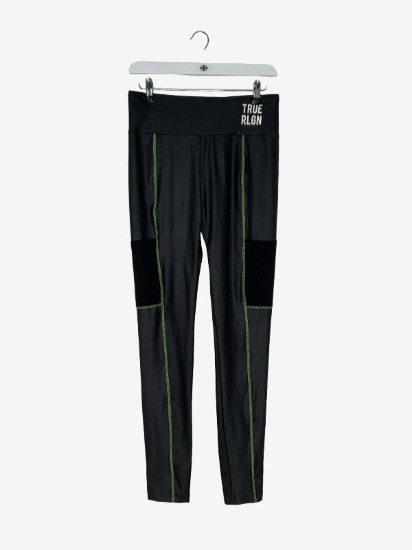 Black athletic leggings with green piping details and a black knee patch, hanging on a white hanger with the brand name 'TRUE RLON' printed in white on the waistband.
