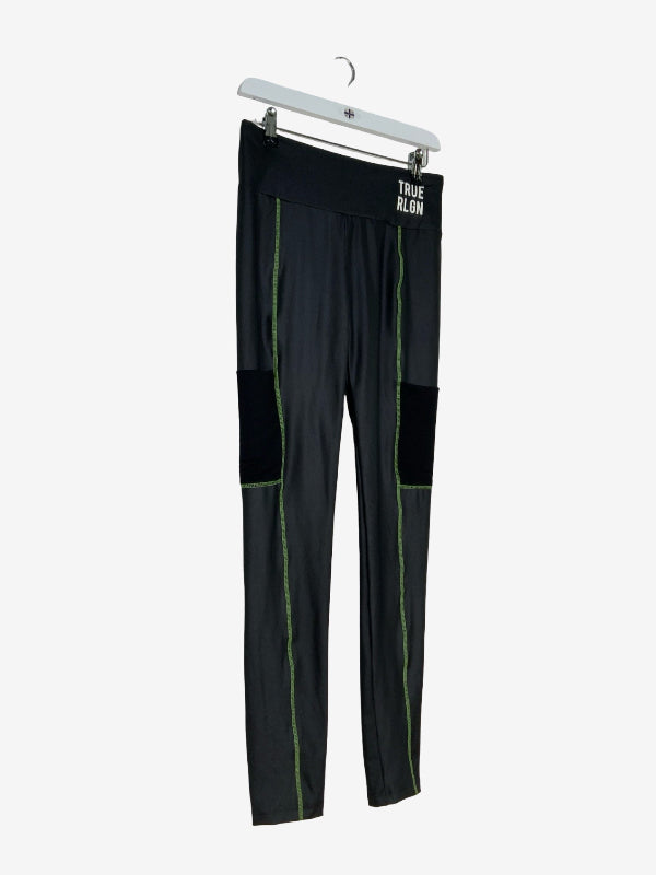 Black athletic leggings with green piping and black knee patches, hanging on a white hanger against a light gray background. The waistband features the text 'TRUE RLGN'.