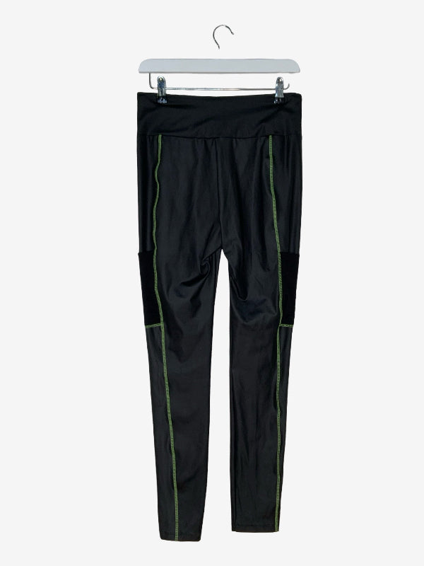 Black athletic leggings with green piping details along the sides, hanging on a white hanger against a light gray background.