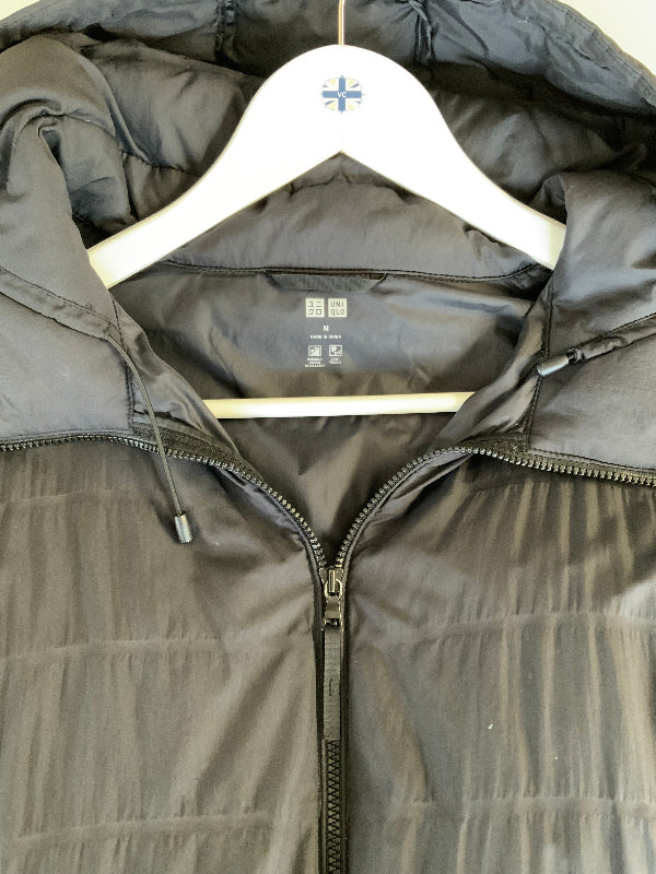  A Black hooded puffer jacket hanging on a white hanger with a small blue cross logo, showing the front zipper and quilted texture.