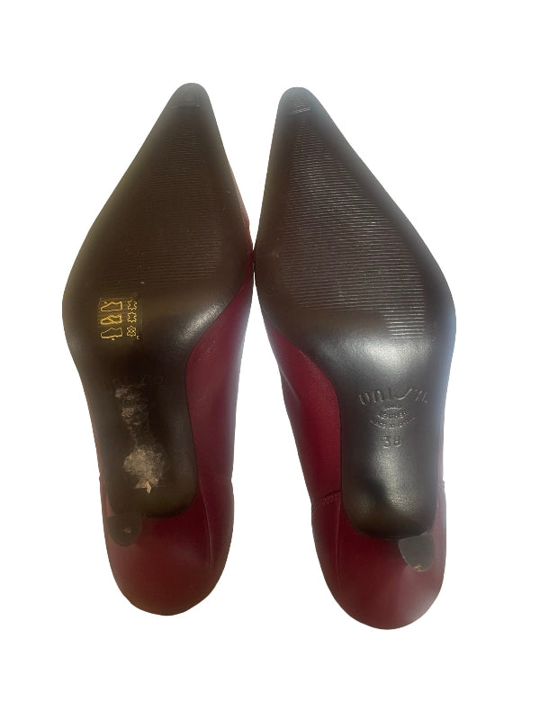 A pair of pointed-toe high heels shown from the sole, featuring a dark brown textured rubber outsole and a reddish-brown heel counter, photographed on a white background.