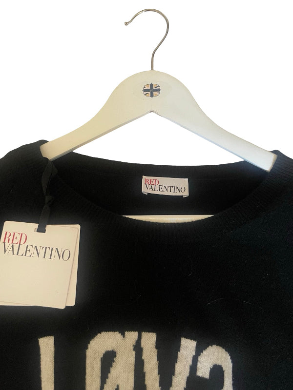 A black knit sweater with a large white 'LOVE' graphic on the front, hanging on a white wooden hanger. The hanger features a small Union Jack logo.