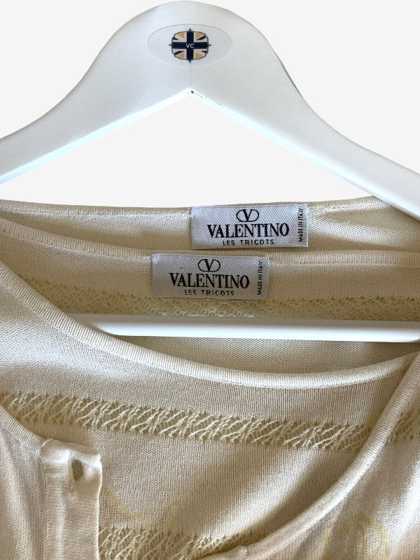 Close-up of a cream-colored Valentino silk blouse on a white hanger, showing the brand labels and fine lace detailing.