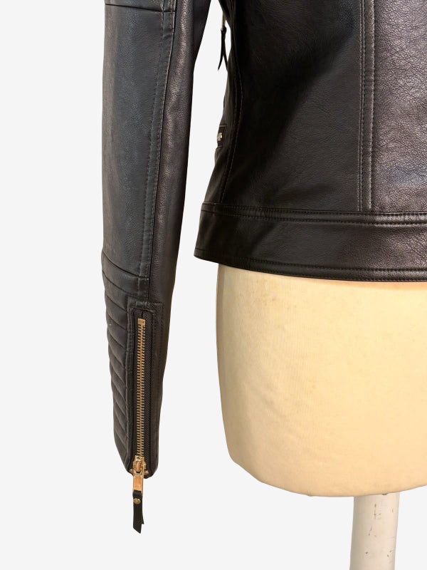 Close-up of a black faux-leather moto jacket on a cream-colored mannequin torso, showing the sleeve with a gold-toned zipper and the side seam of the jacket.