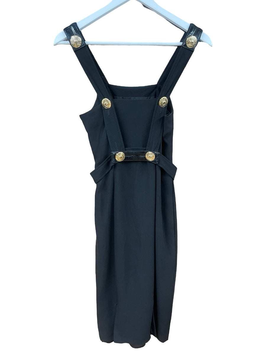 A dark  black pinafore-style dress with gold-tone decorative buttons, hanging on a white hanger against a plain white background.