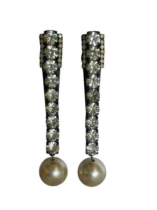 A pair of long drop earrings featuring rows of clear faceted rhinestones set in a dark metal frame, with a large round pearl hanging from each earring, shown against a plain white background.