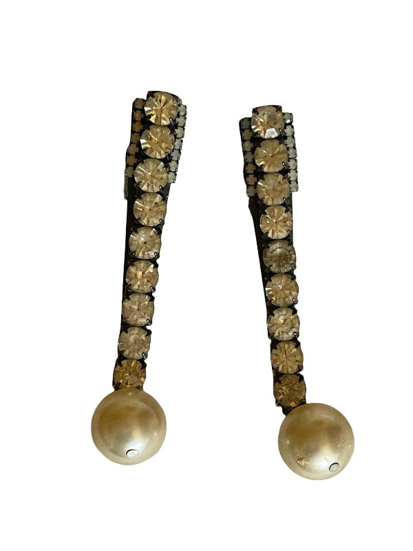 A pair of long drop earrings featuring a vertical row of round champagne-colored rhinestones on a dark setting, terminating in a large champagne pearl at the bottom, shown against a plain white background.