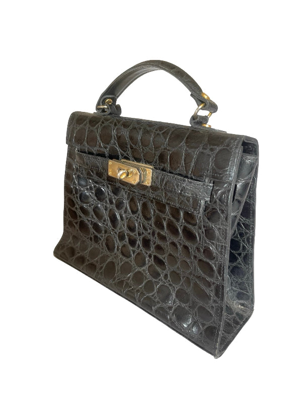 A structured black crocodile-embossed leather handbag with a top handle and gold-tone hardware, shown against a plain white background.