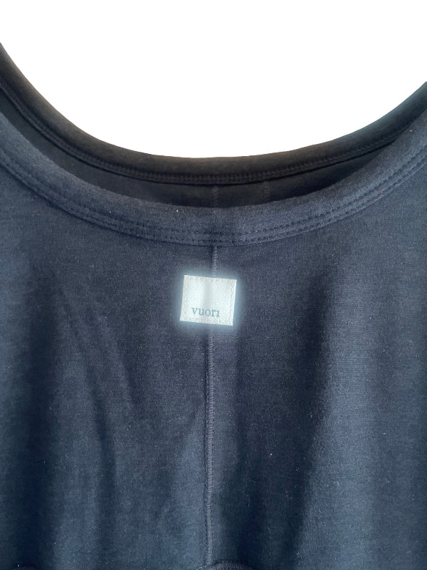 Close-up of a black crewneck jumpsuit with a small white brand label reading 'Vuori' visible at the back