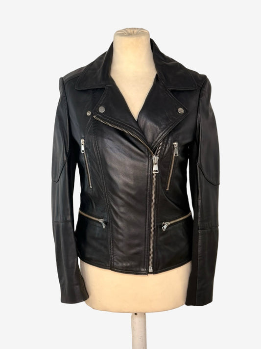 A black leather moto jacket with silver zippers and snap details, displayed on a beige mannequin torso against a light gray background.